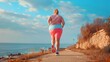 An overweight woman running on the path by the sea, low angle shot from behind. Weight loss concept.