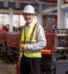 Senior engineer wears white protective helmet standing in heavy machine metalwork factory looking at camera. Mature technician skillful manufacturing manager investigate workshop for safety production