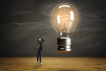 Poster - Thoughtful young businesswoman with glowing light bulb in modern room with wooden flooring. Success, idea and innovation concept.