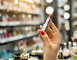 Woman’s hand with red nail polish holding pink lipstick in a beauty shop