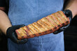 chef in blue apron holding a grilled rib rack