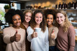 Portrait of five happy girls shows thumbs up who met in a cafe, girls of different nationalities.