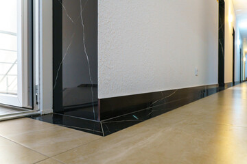 The detail of the corner baseboard on the wall and granite tiles on the floor. A white wall with a copy space, decorated with decorative bricks and baseboards. Interior design in a office building.