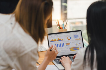 Two businesspeople or an accountant team are analyzing data charts, graphs, and a dashboard on a laptop screen in order to prepare a statistical report and discuss financial data in an office.