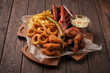 hearty assortment of appetizers, including crispy onion rings, golden fries, grilled sausages, glazed chicken wings, and creamy coleslaw, is beautifully presented on a rustic wooden board