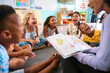 © Monkey Business - Female Primary Or Elementary School Teacher Reads Story To Multi-Cultural Class Seated In Classroom
