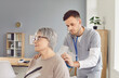 © Studio Romantic - Young male nurse attending to senior woman patient. Man doctor in scrubs uses stethoscope to examine heart and lungs of old lady who came to clinic for routine medical checkup