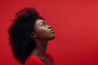 Portrait of a confused puzzled minded African American young woman in red tank top isolated on a red background, with copy space. Contemplation doubt concept