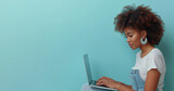 Fototapeta Młodzieżowe - Laptop in hands of happy 35 years black woman freelancer wearing white t-shirt, sitting on blue background. Concept of freelance, studying, IT technology, cyberspace