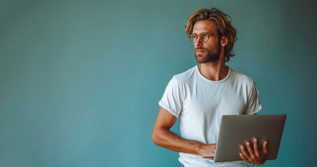 Laptop in hands of happy 35 years man freelancer wearing white t-shirt looking away on blue background. Concept of freelance, studying, IT technology, cyberspace