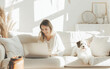 Woman works on laptop computer while sitting with her cute dog on a couch at home. Remote work from home and friendship with pets. Distant online work, animals and people concept. 