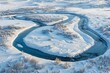 A river winds through a field blanketed in snow, creating a stark contrast between the cold white landscape and the flowing water