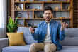 © Liubomir - Confused man sitting with phone on sofa at home