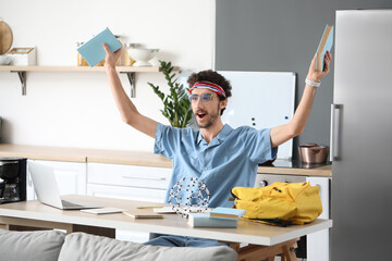 Canvas Print - Happy male student with books sitting at table in kitchen