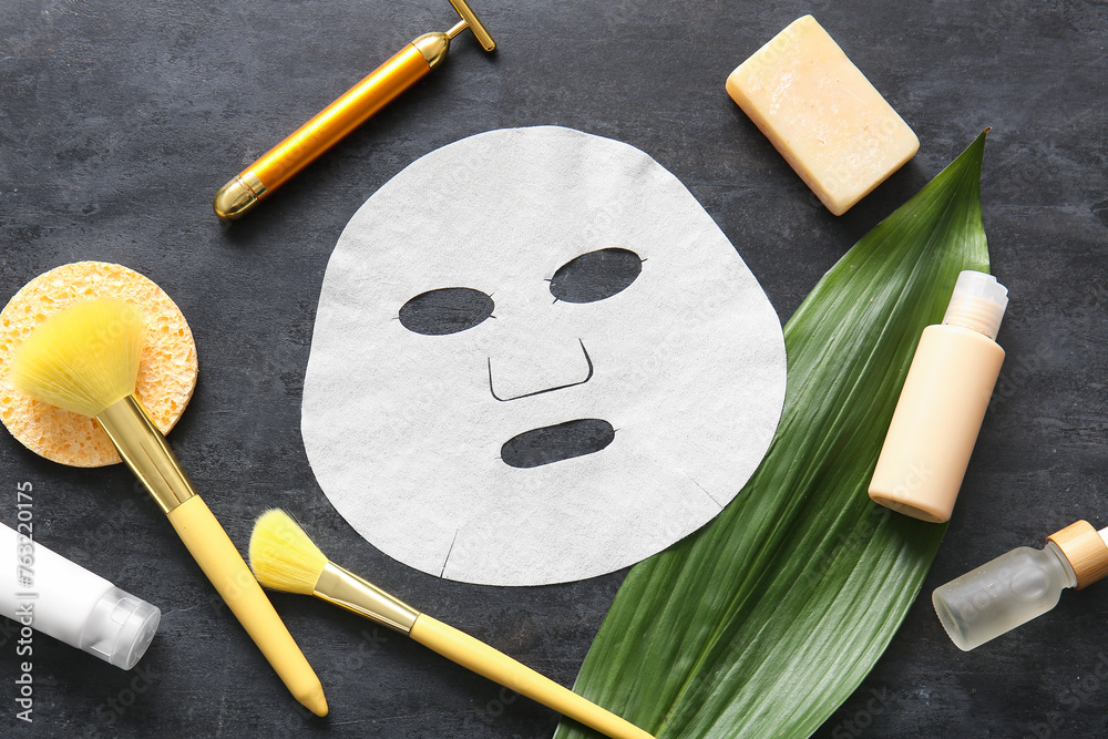Facial sheet mask with different cosmetic products and leaf on black background