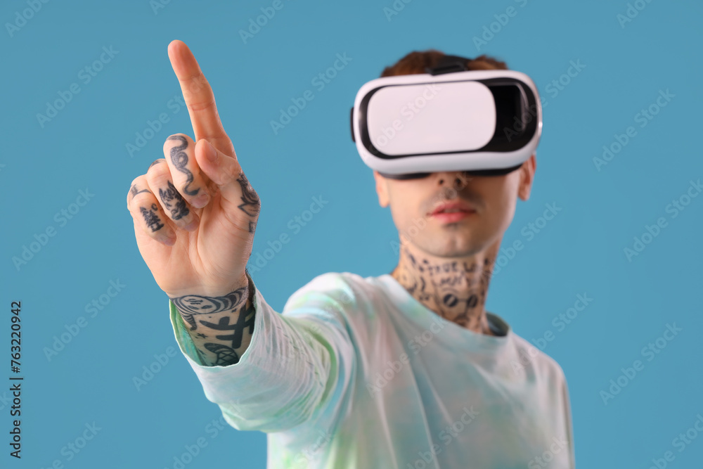 Young man in VR glasses using virtual screen on blue background, closeup