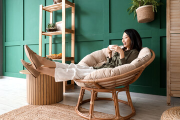 Sticker - Young Asian woman with coffee cup sitting in armchair at home