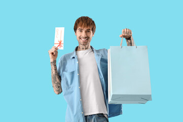 Poster - Young tattooed man with gift card and shopping bags on blue background