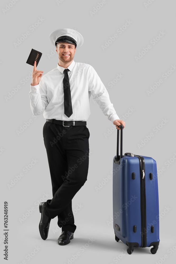 Male pilot with passport and suitcase on light background