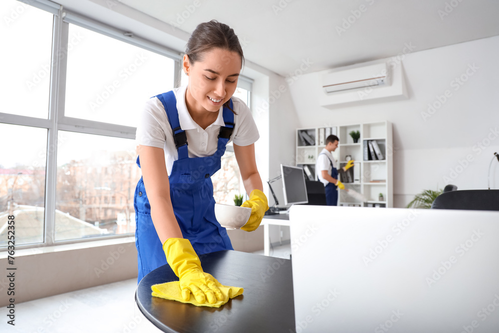 Female janitor cleaning table in office