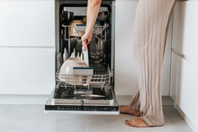 female hands turn on the dishwasher with dirty dishes in a white kitchen