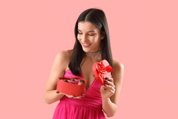 Sticker - Young woman with box of heart-shaped chocolate candies on pink background