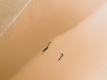 Aerial View Of A Two Surfers And Their Shadows On A Golden Beach In Peniche, Portugal.