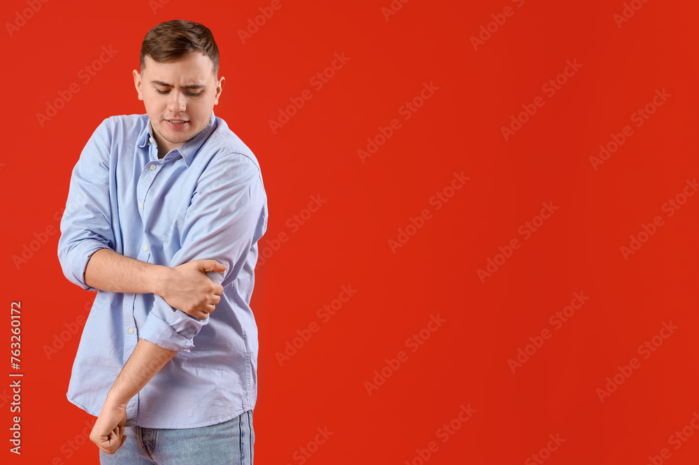 Young man suffering from arm pain on red background