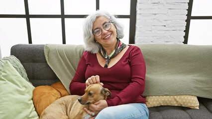 Sticker - A grey-haired woman enjoys a moment with her dog on a comfortable couch in a cozy living room.