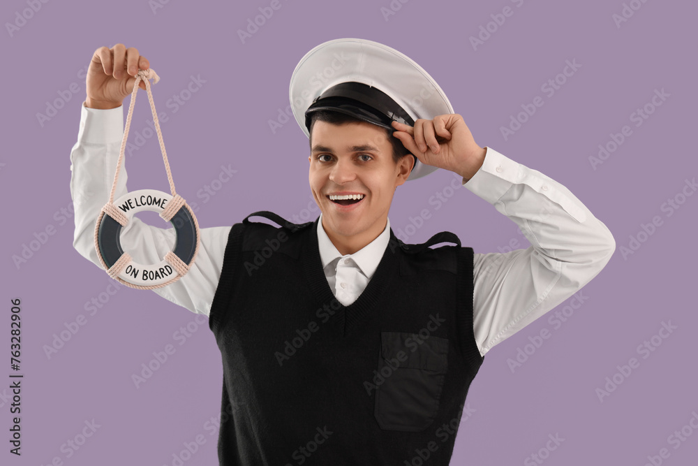 Young sailor with small ring buoy on lilac background