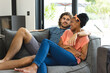 A diverse couple is relaxing together on a gray sofa at home