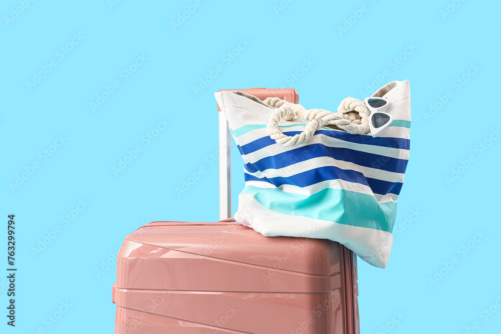 Suitcase with beach bag on blue background, closeup