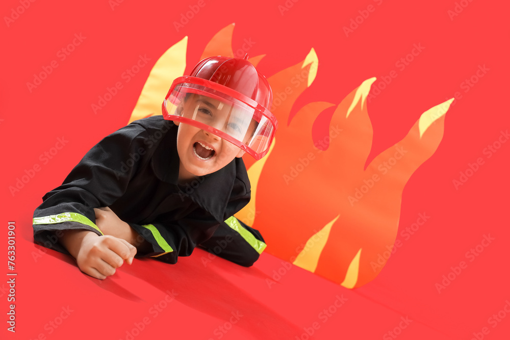 Scared little firefighter lying against paper flame on red background