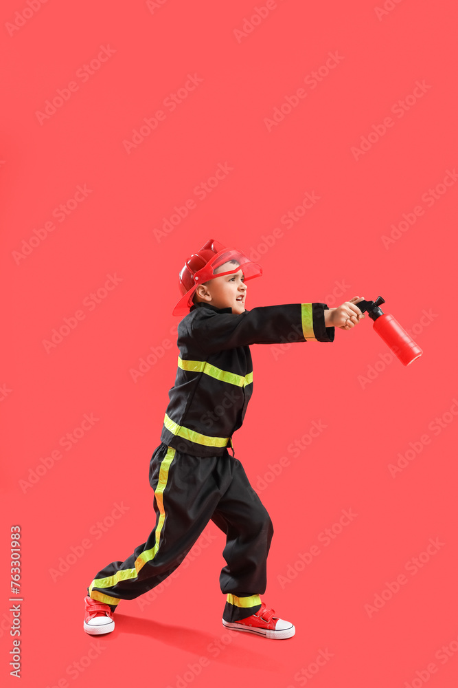 Cute little firefighter with toy extinguisher on red background