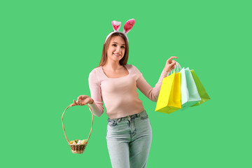 Poster - Young woman in bunny ears with shopping bags and Easter eggs on green background