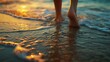 A person's feet are in the water, with the sun setting in the background