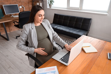 Wall Mural - Pregnant businesswoman working with laptop at table in office