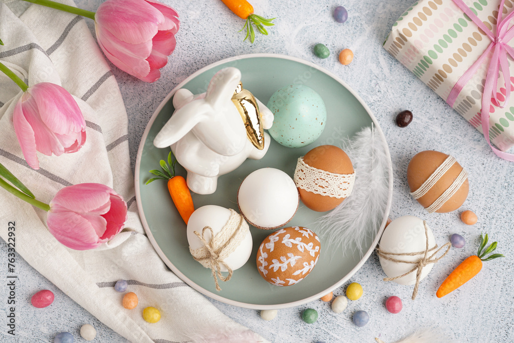 Plate with decorated Easter eggs, toy bunny and tulips on white background
