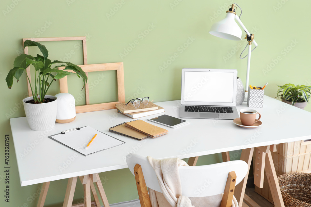 Workplace with stationery, lamp, clipboard and laptop in light office