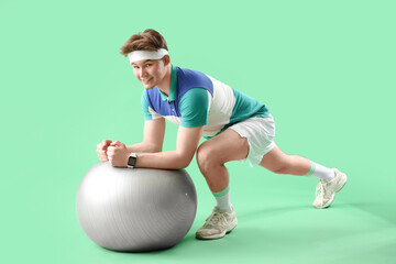 Wall Mural - Sporty young man training with fitball on green background