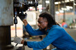 © KANGWANS - A man with dreadlocks is looking at a drill. The man is wearing a blue shirt and a blue jacket