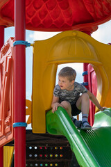 Wall Mural - A curious child on top of a colourful slide in a playground looking into the distance