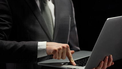 Wall Mural - A businessman works with a laptop in close-up in a dark office