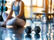 A woman is sitting on the floor in fitness , next to her there is an iron dumbbell and water bottle, blurred background of gym, low angle shot