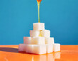 Pile de carrés de sucre en pyramide, fond bleuté support orange, miel qui coule 