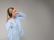 Blonde smiling woman using headphones side profile listening to music. Blue oversize shirt. Gray background copy space