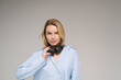 Blonde beautiful young woman with headphones and blue shirt looking at camera. Studio shoot. Gray plain background. Music lover theme banner with copy empty space