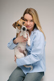 Fototapeta Konie - Woman hugging dog portrait. Adorable friends studio portrait. Blonde girl holding her pet Jack Russell terrier, sitting on the floor in photo studio
