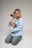 Fototapeta Konie - Woman hugging dog. Adorable friends studio portrait. Blonde girl holding her pet Jack Russell terrier, sitting on the floor in photo studio