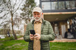 © Miljan Živković - One senior man stand in front of tiny house in day use smart phone